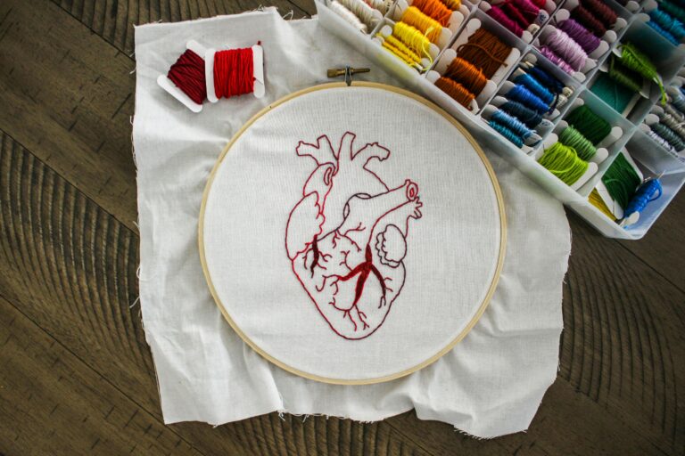 Close-up of an anatomical heart embroidery with vibrant threads on a wooden table.